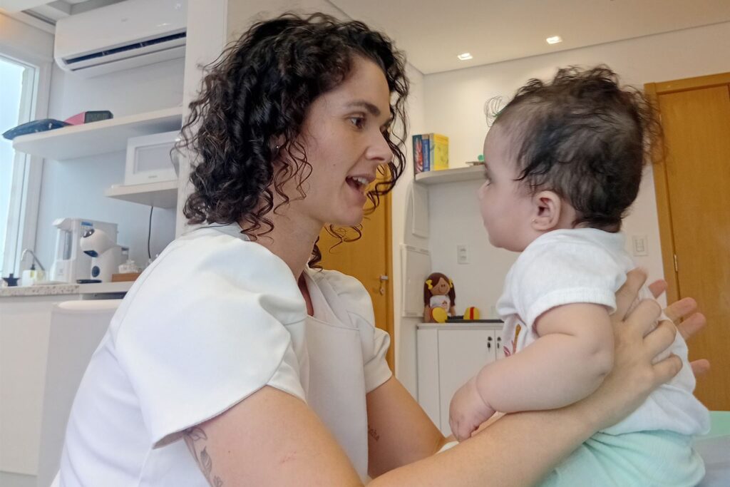 Fisioterapeuta conversando com um bebê sentado na maca durante atendimento na Clínica AmarElo