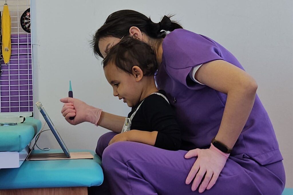 Fonoaudióloga e criança olhando juntas para um tablet durante atendimento de fonoaudiologia na Clínica AmarElo