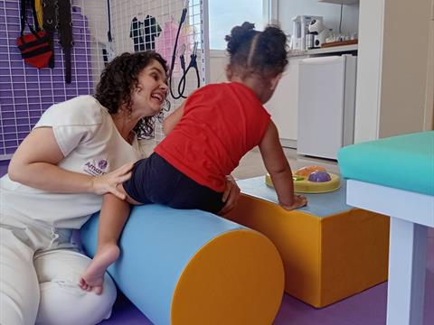 Fisioterapeuta da Clínica AmarElo auxiliando criança em atividade motora com rolo terapêutico