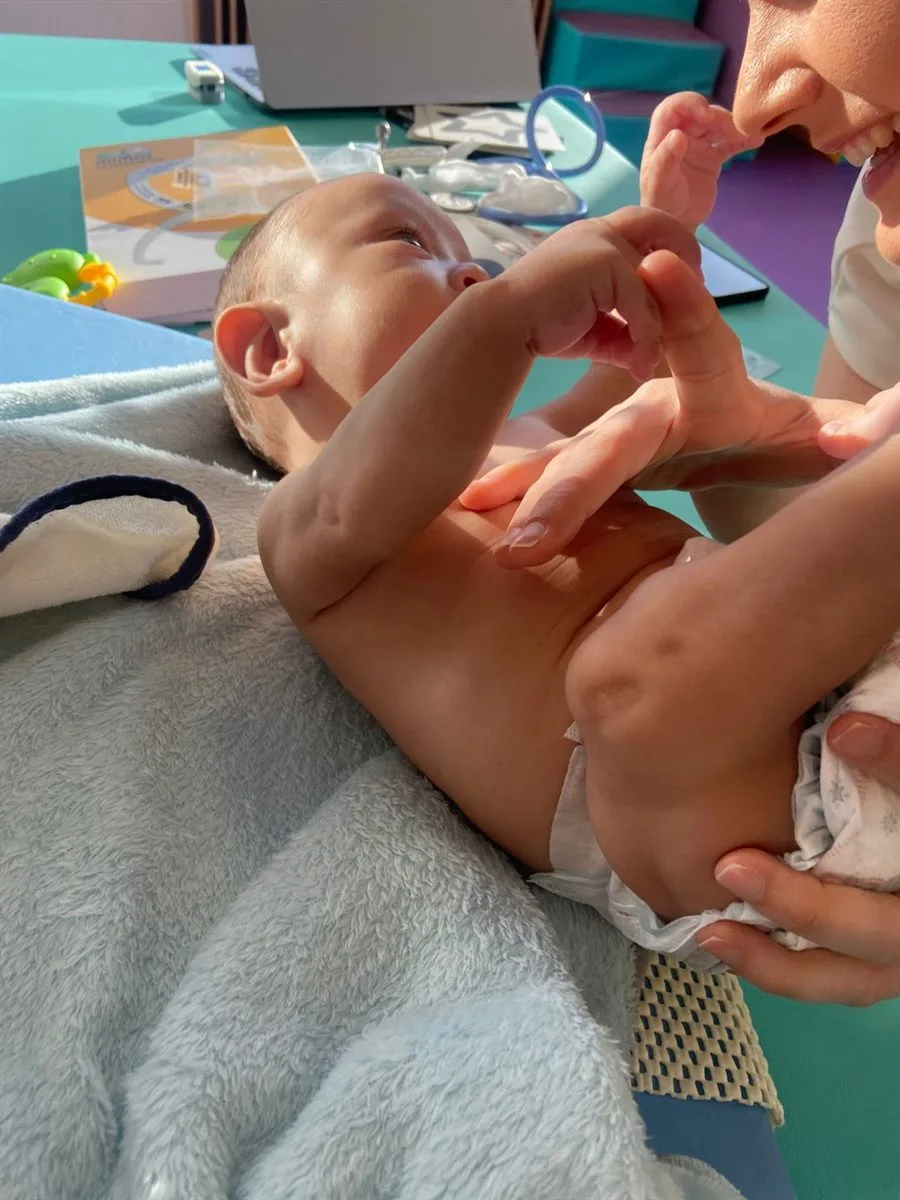 Bebê deitado em uma manta recebendo estímulo nas mãos durante atendimento de fisioterapia infantil